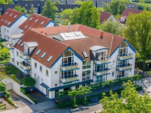 Een meerlaags woongebouw met een rood pannendak, balkons en een tuingedeelte.
