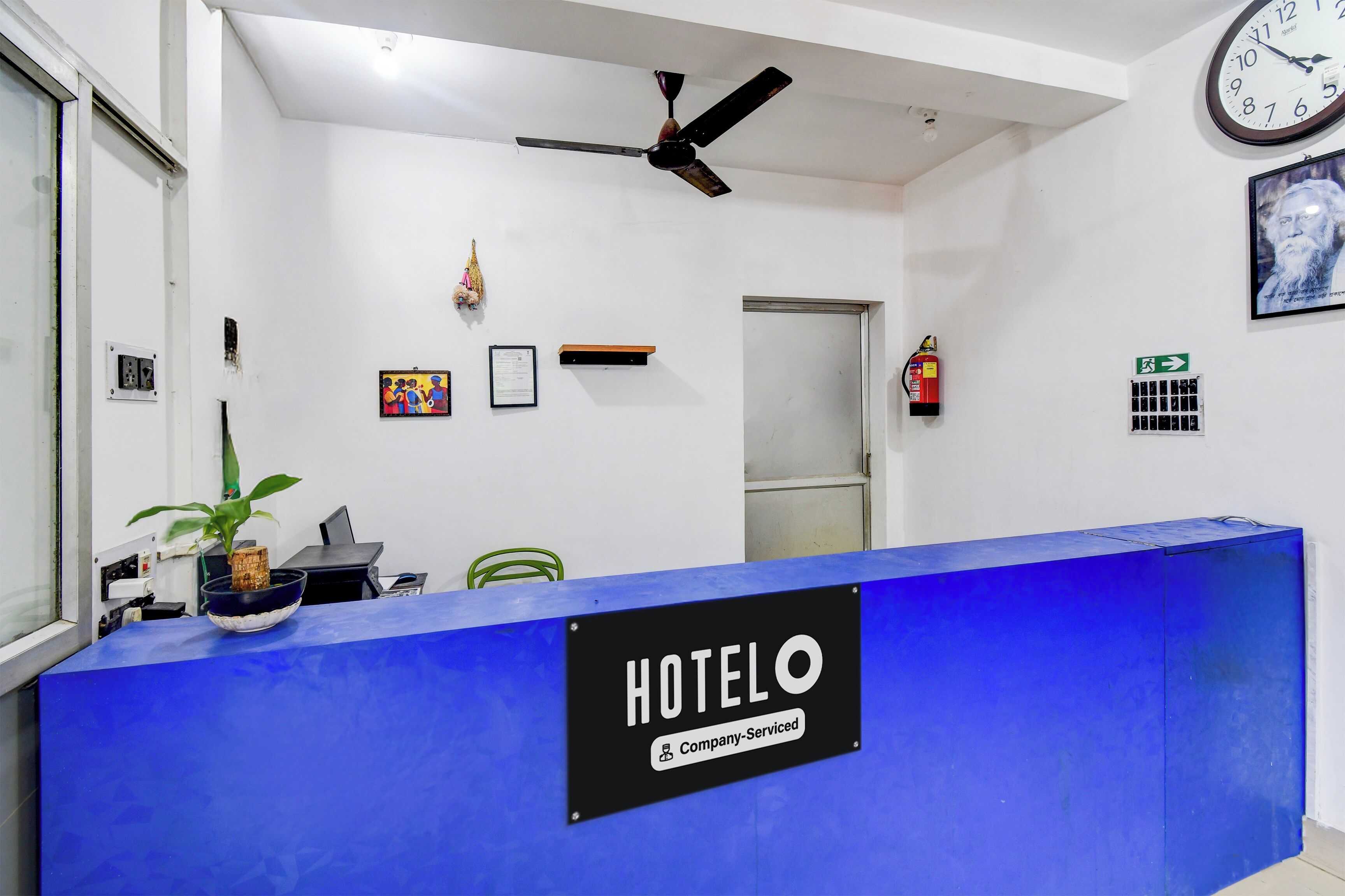 A hotel reception desk with a blue counter, a clock, and a fire extinguisher.