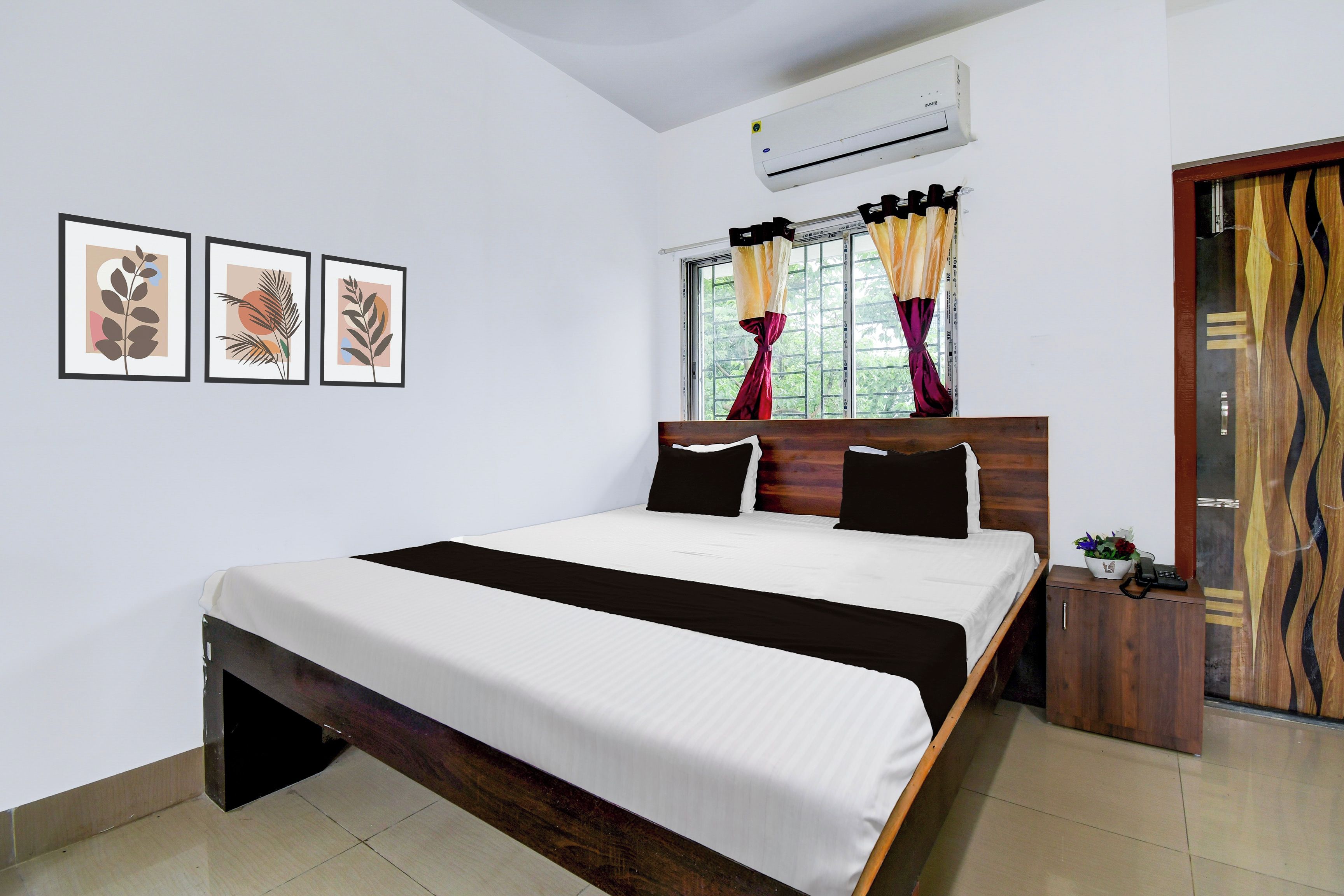 A bedroom with a bed, a nightstand, a telephone, and a window with curtains.