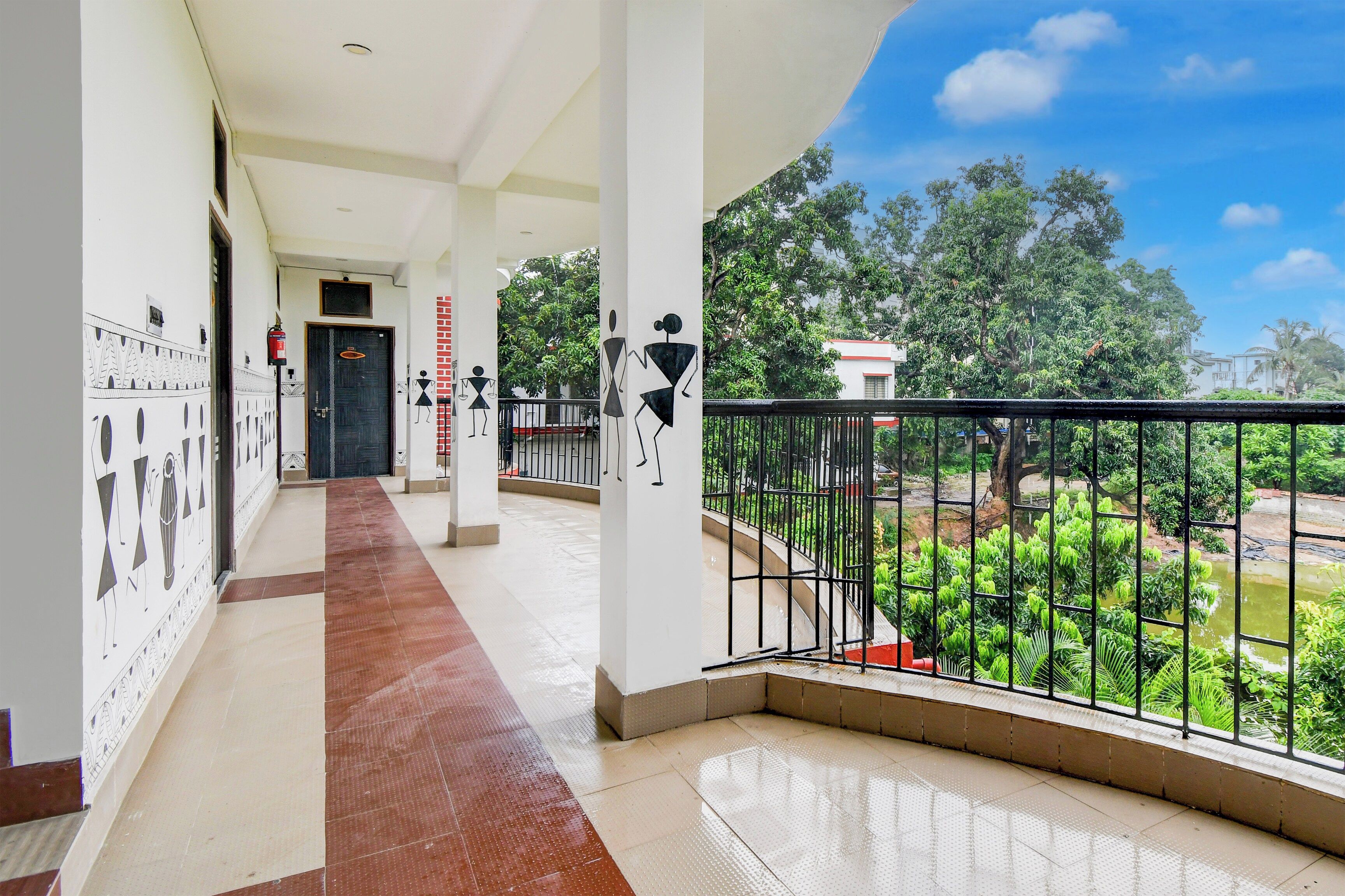 A corridor with a tiled floor leading to a balcony with a metal railing overlooking a garden.
