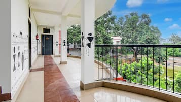 A corridor with a tiled floor leading to a balcony with a metal railing overlooking a garden.