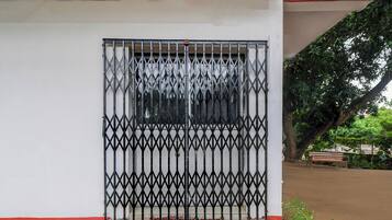 Una reja metálica con un diseño geométrico, un muro rojo y blanco, y un banco en un entorno similar a un parque.