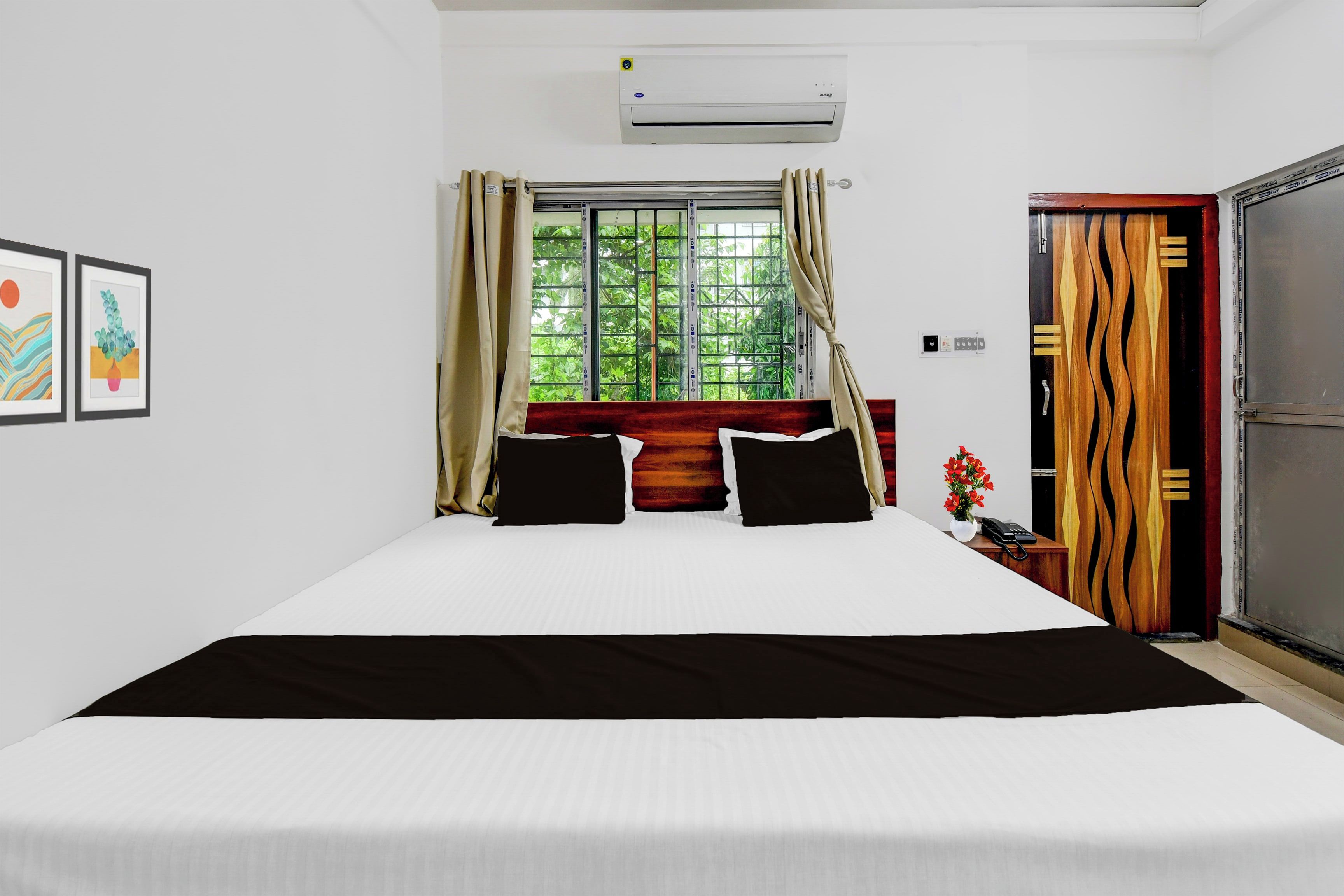 A hotel room with a bed, a window with curtains, an air conditioning unit, and a door with a unique design.