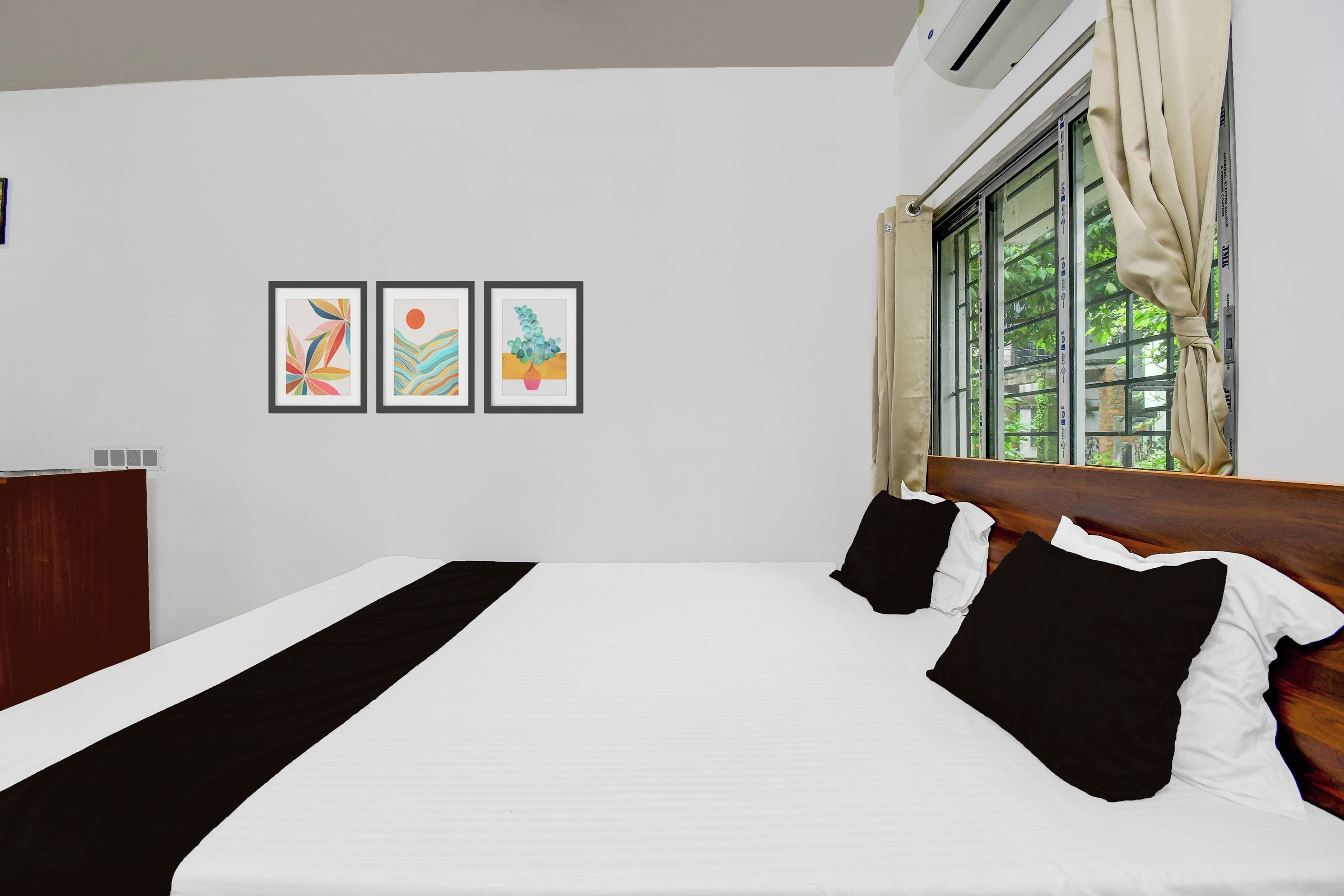 A bedroom with a bed, a window with curtains, and three framed artworks on the wall.
