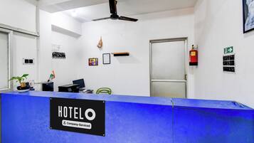 Balcão de recepção de hotel com bancada azul, ventilador de teto e extintor de incêndio na parede.