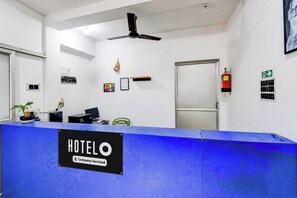 A hotel reception desk with a blue counter, a ceiling fan, and a fire extinguisher on the wall.
