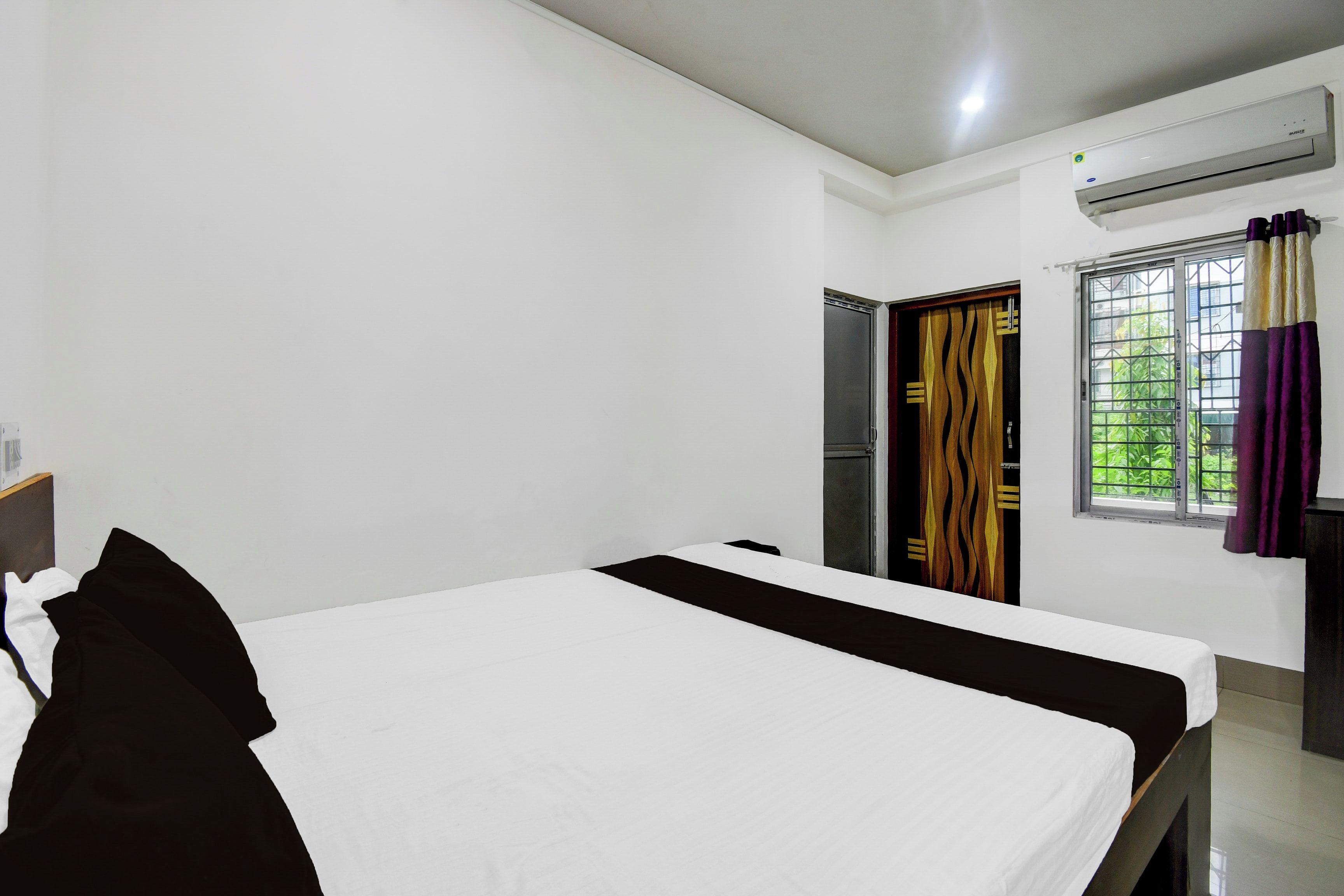 A hotel room with a bed, a wardrobe, a window with curtains, and an air conditioning unit.