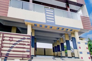 Un edificio de varios pisos con un diseño arquitectónico moderno, que destaca por una entrada con fachada de vidrio y una puerta metálica.