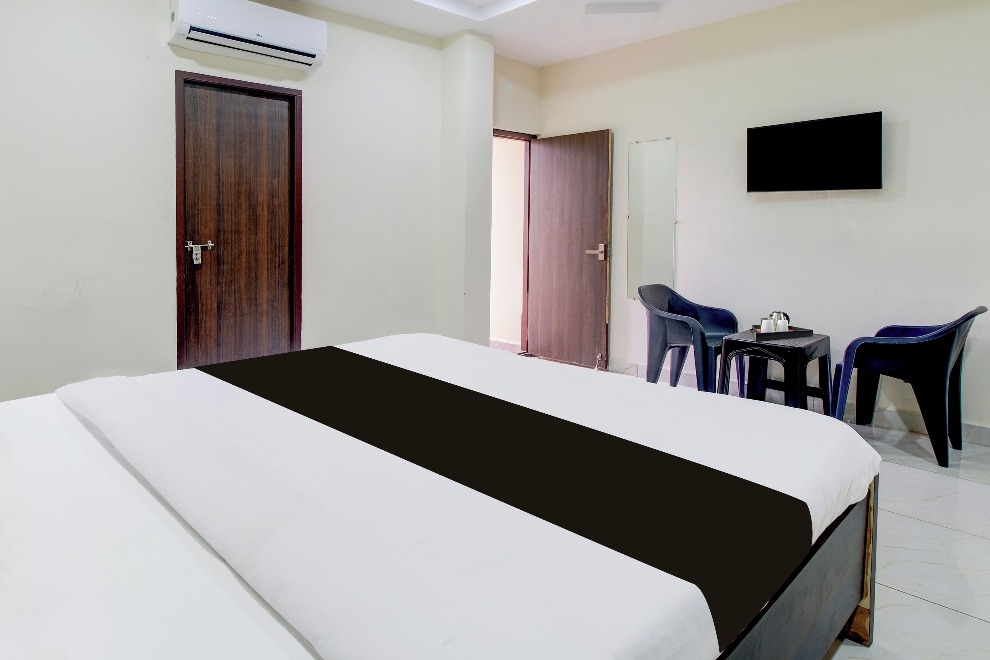 Quarto de hotel com cama, escrivaninha, duas cadeiras e televisão na parede.