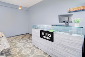 Un comptoir d’accueil d’hôtel avec une cloison en verre, une enseigne indiquant qu’il s’agit d’un hôtel proposant des services aux entreprises, et un sol à motifs.