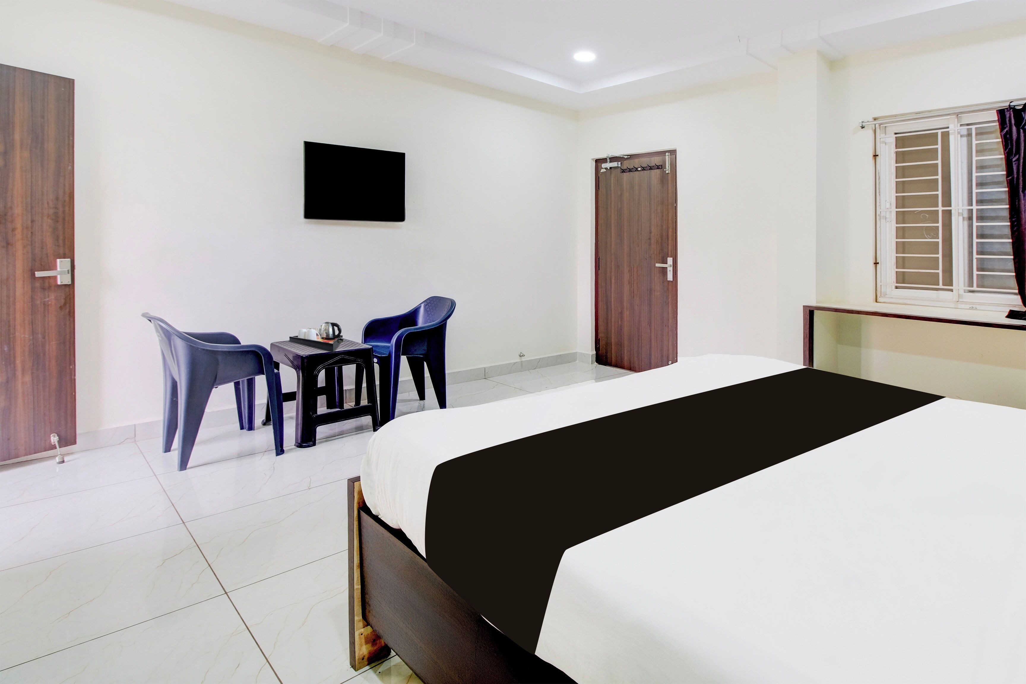 A hotel room with a bed, a desk with chairs, a television, and two wardrobes.