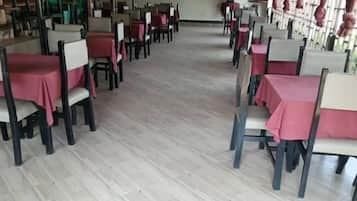 Un restaurante con filas de mesas y sillas, piso de baldosas y techo alto.