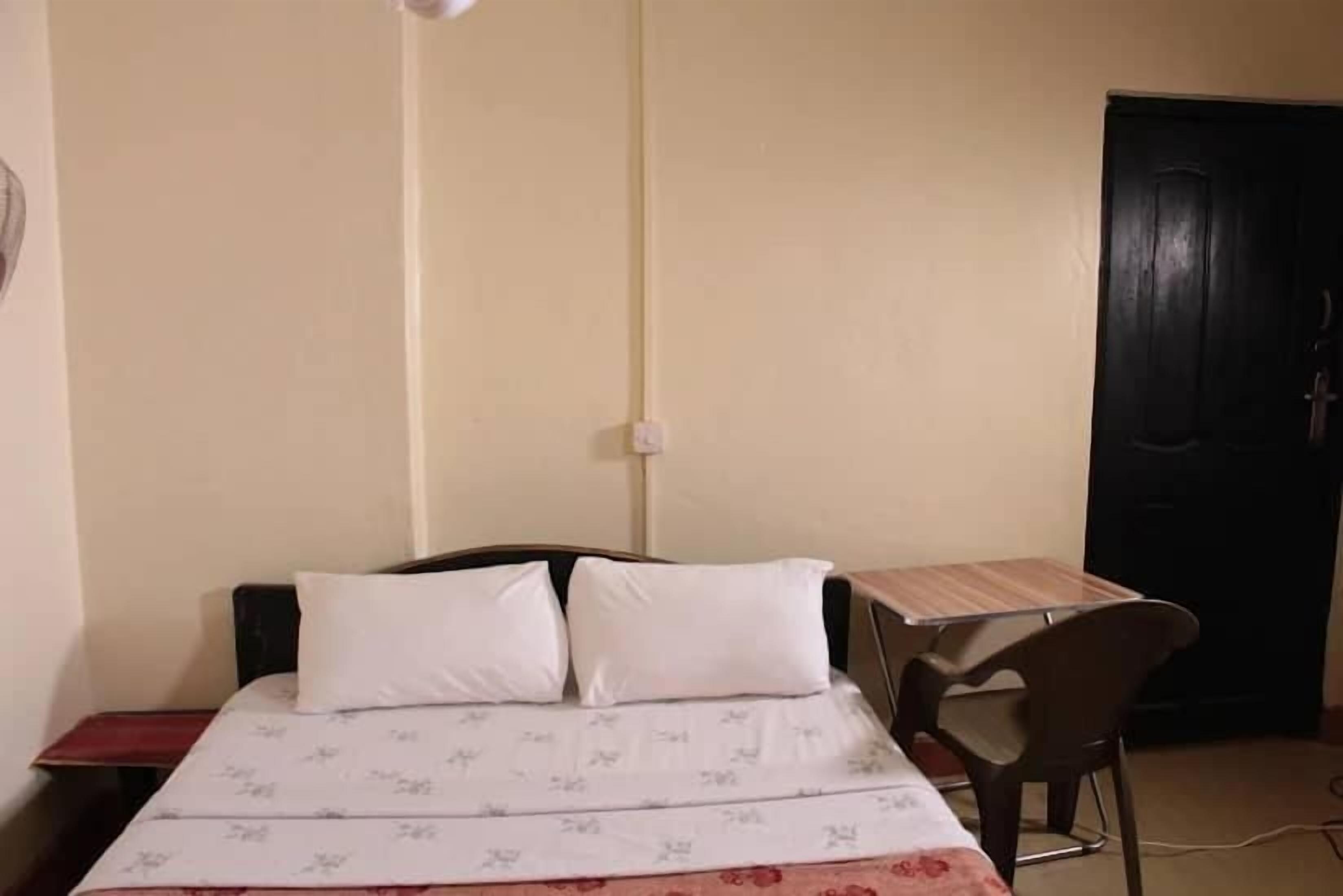 Quarto com cama, cadeira, escrivaninha e porta.