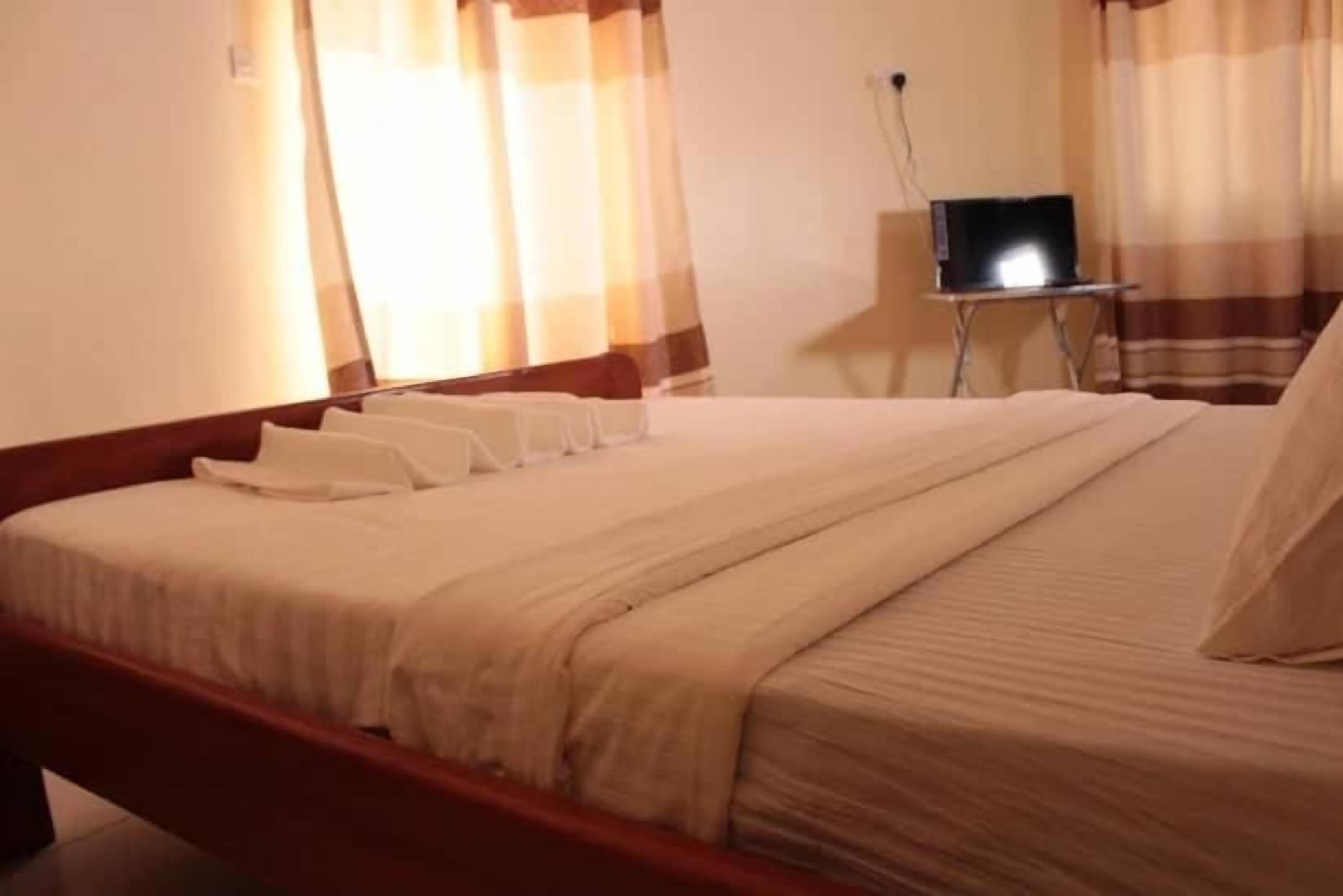 A neatly made bed with a wooden frame, a bedside table with a lamp, and a laptop on the table.