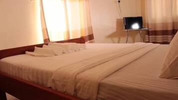 A neatly made bed with a wooden frame, a bedside table with a lamp, and a laptop on the table.