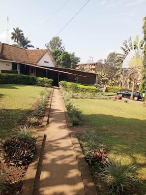A pathway leading to a building with a tiled roof, surrounded by a well-maintained lawn and various plants.