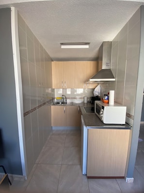 A compact kitchen with a microwave, sink, and wooden cabinets. - Los Boliches one-bedroom apartment with a lift, Beach 130m, Train st. dist.0.8m (Fuengirola)