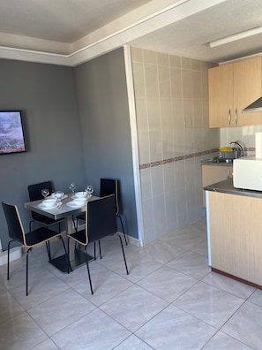 A dining area with a table set for four, a kitchen with wooden cabinets, and a tiled floor. - Los Boliches one-bedroom apartment with a lift, Beach 130m, Train st. dist.0.8m (Fuengirola)