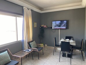 A room with a dining table, chairs, a television mounted on the wall, a window with curtains, and a potted plant. - Los Boliches one-bedroom apartment with a lift, Beach 130m, Train st. dist.0.8m (Fuengirola)