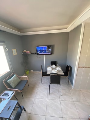 Un coin repas avec une table dressée pour quatre personnes, un téléviseur fix é au mur et une fenêtre sur le côté gauche.