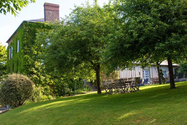 A grassy area with a building partially covered in ivy, a statue, and outdoor furniture.