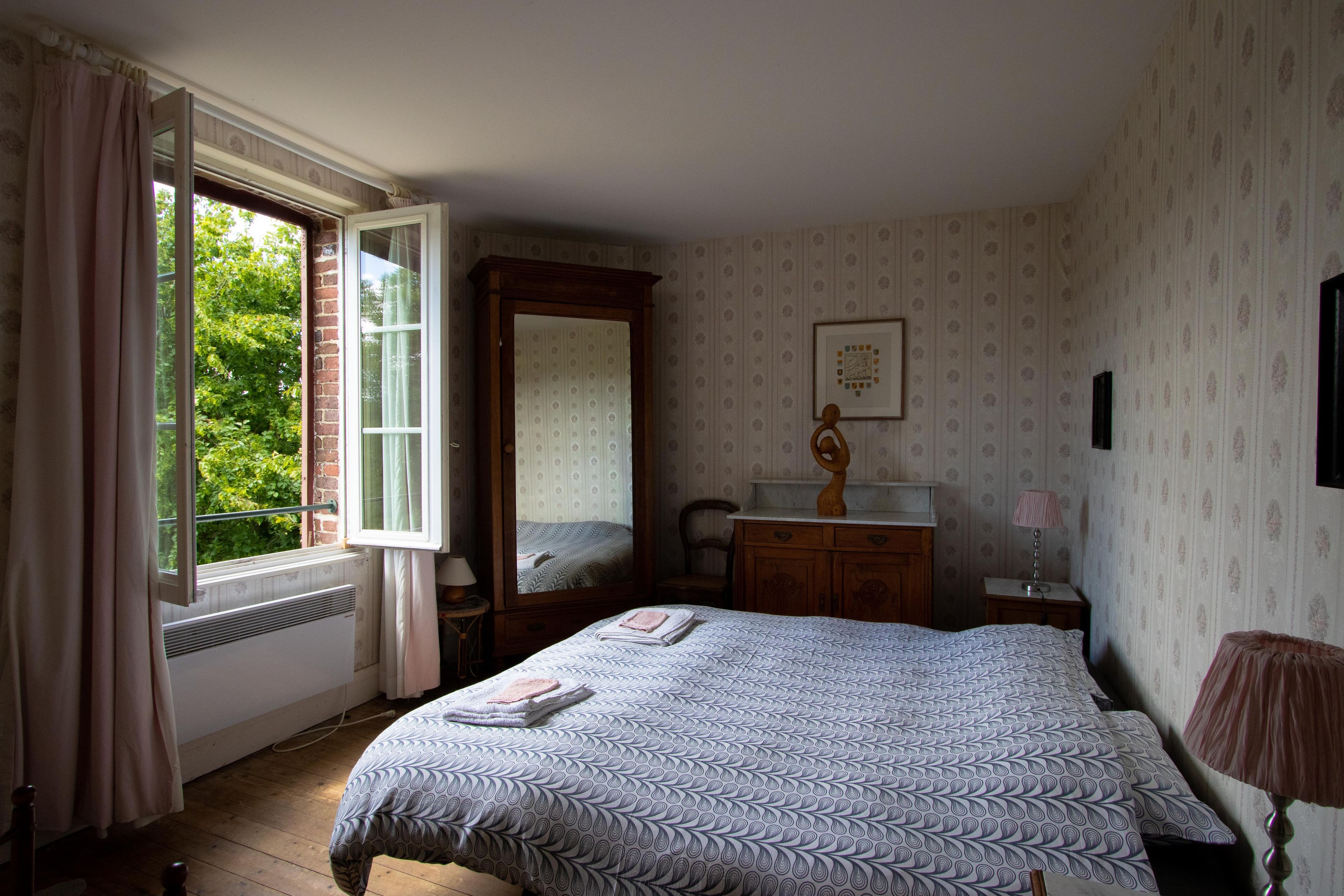 Un dormitorio con cama, cómoda, espejo, ventana con cortinas e imagen enmarcada en la pared.