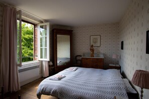 A bedroom with a bed, a dresser, a mirror, a window with curtains, and a wall with a framed picture.