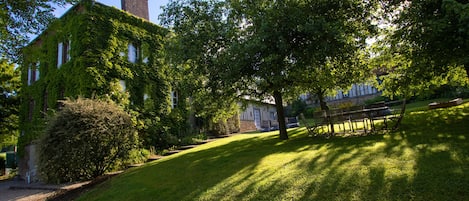 A building with ivy-covered walls and a chimney, surrounded by a well-maintained lawn and trees.