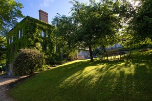 A building with ivy-covered walls and a chimney, surrounded by a well-maintained lawn and trees.