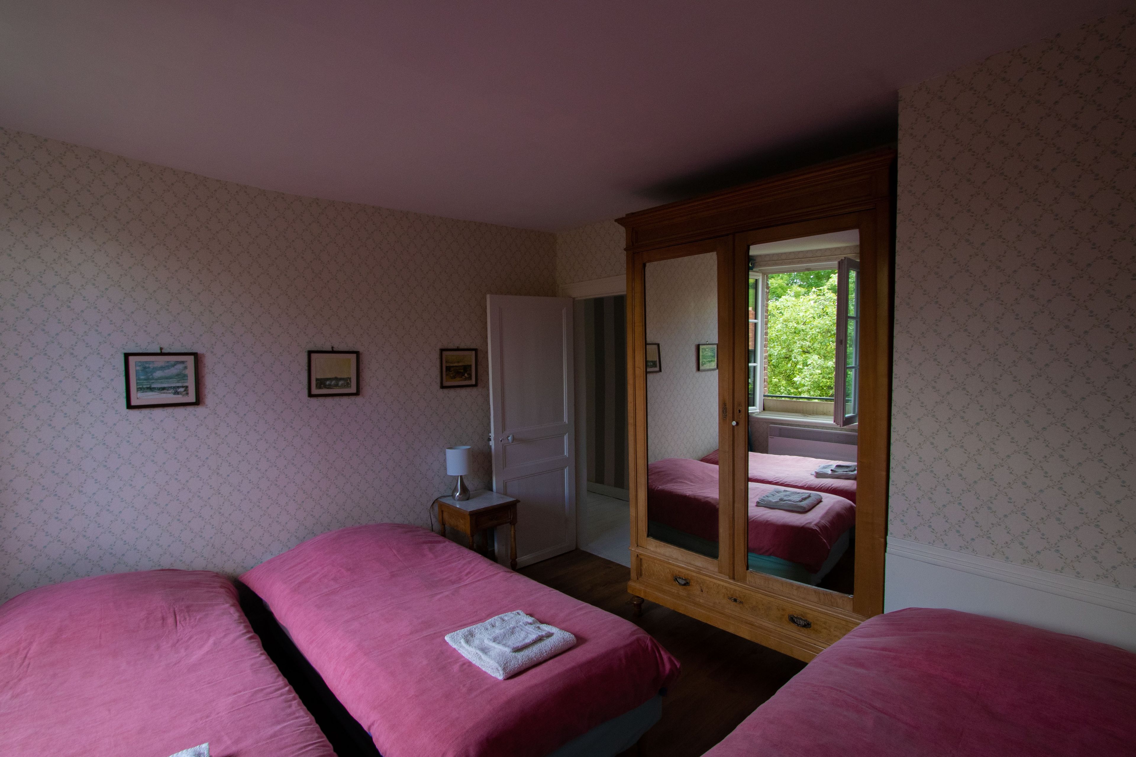 Een hotelkamer met twee bedden, een garderobe, een spiegel en een klein tafeltje met een lamp.