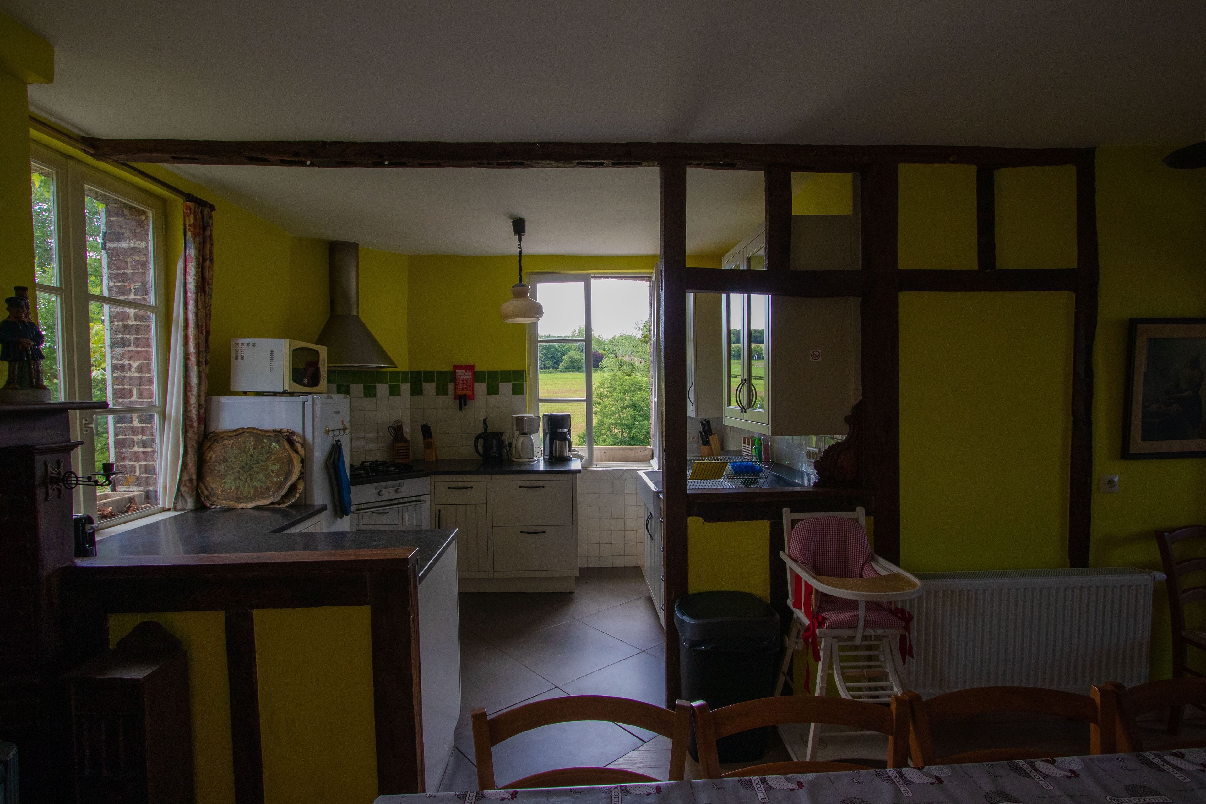 Una cocina con vistas al jardín, una zona de comedor con mesa y sillas, y un ventanal con cortinas.