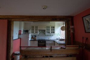 Ett kök med vita skåp, en mikrovågsugn, en spis och ett kylskåp.