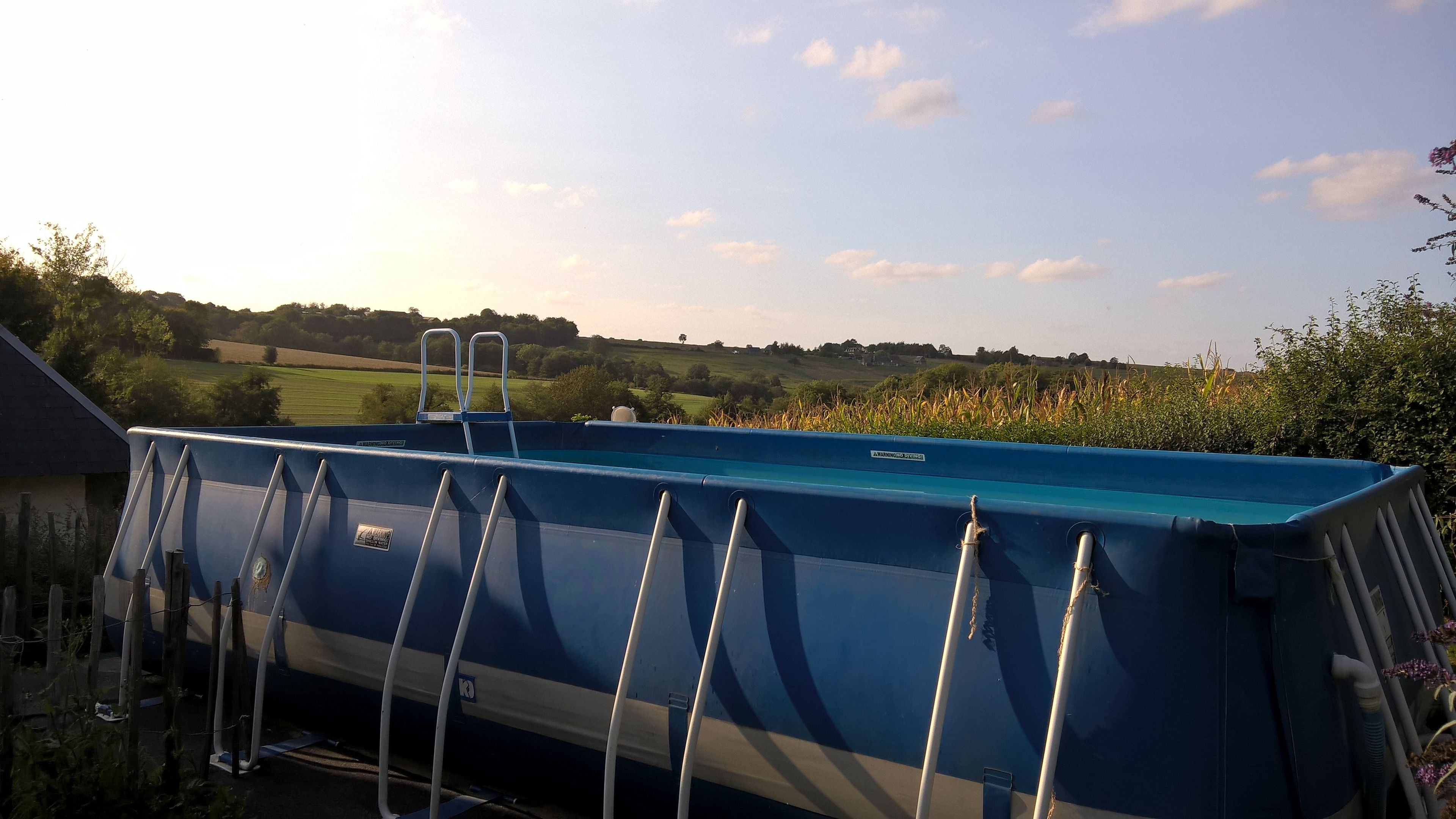Une piscine bleue avec des échelles, entourée d’un paysage rural.