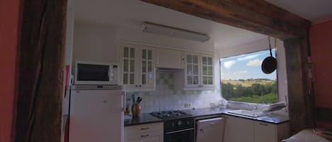 A kitchen with white cabinets, a stove, and a window with a view of the countryside.