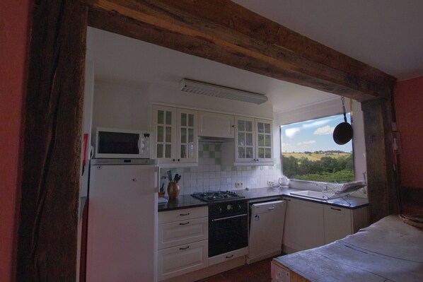 A kitchen with white cabinets, a stove, and a window with a view of the countryside.