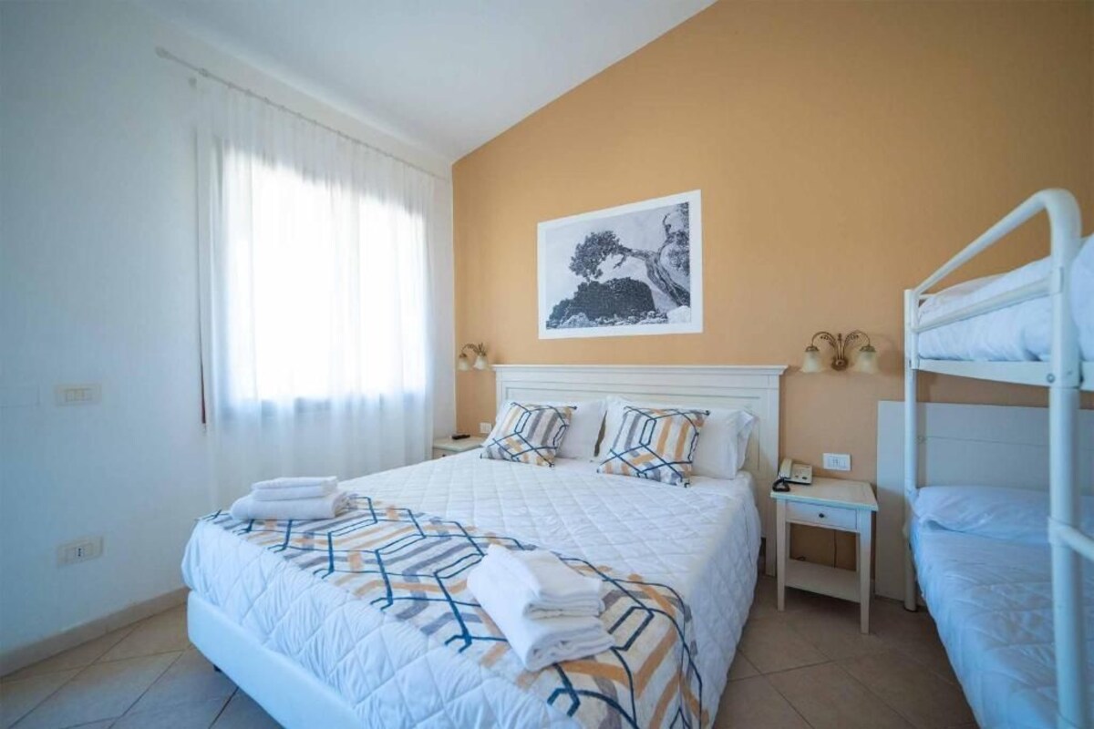Una habitación de hotel con cama, mesita de noche, lámpara y literas.