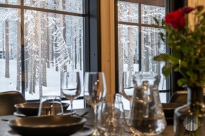 A table set with clear glassware and a pitcher, with a view of a snowy forest through a window. - Yläkasi C by Holiday in Lapland (Levi)