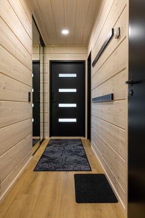 Een gang met een houten vloer, een zwarte deur met verlichte panelen en een zwart tapijt bij de ingang.