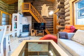 A log cabin interior with a stone fireplace, wooden staircase, and a television.
