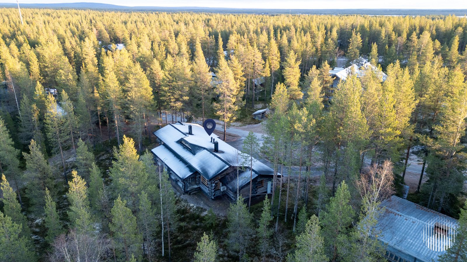 En stuga omgiven av tät skog, med ett tak av metall och en liten, intilliggande byggnad.