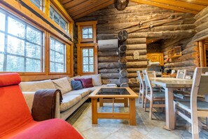 A log cabin interior with a sofa, dining table, chairs, and a kitchen area.