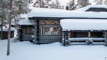 Une cabane en rondins dont le toit et les fenêtres sont recouverts de neige, entourée d’arbres.