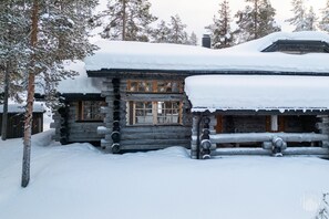 A log cabin with a snow-covered roof and windows, surrounded by trees.