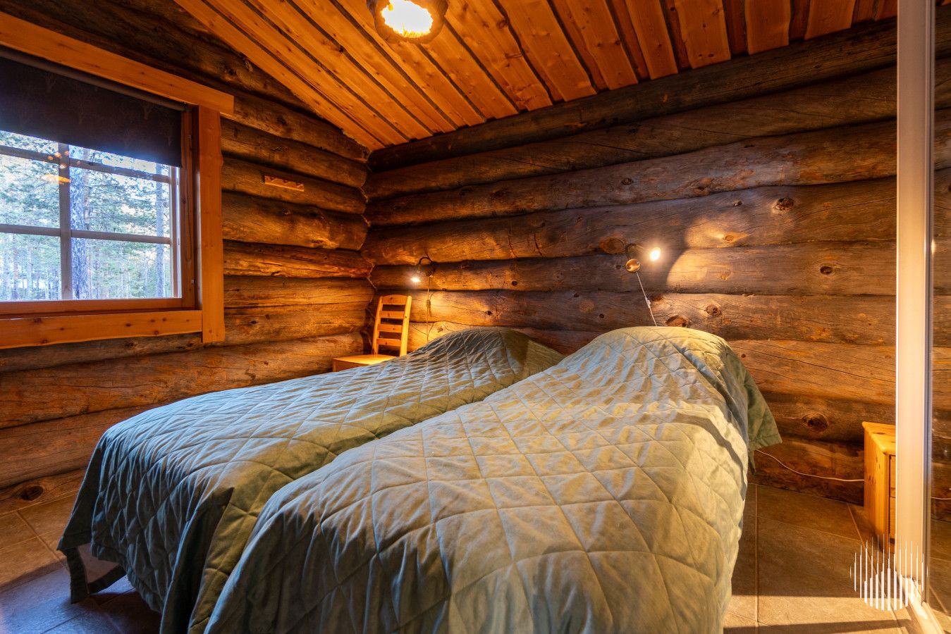 Une chambre dans un chalet en rondins, avec deux lits, une fenêtre et un plafond en bois.
