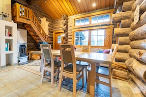A log cabin interior with a dining area, wooden staircase, and a fireplace.