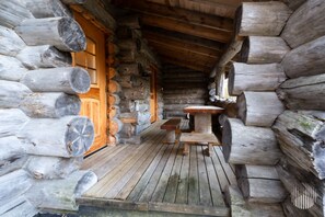 A log cabin interior with a wooden bench and a table, a wooden door, and a wooden ceiling.