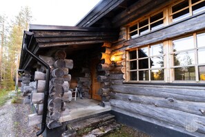 A log cabin with a wooden door, a porch with a bench, and a window with a view of the surrounding forest.