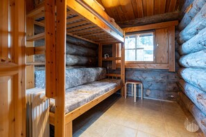 A log cabin interior with a bunk bed, a small stool, and a window.