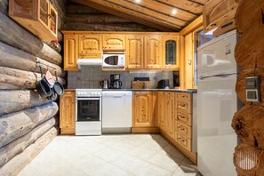 A log cabin kitchen with wooden cabinets, a microwave, stove, and refrigerator.