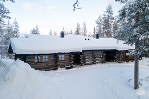 A log cabin with a snow-covered roof, surrounded by snow-covered trees.